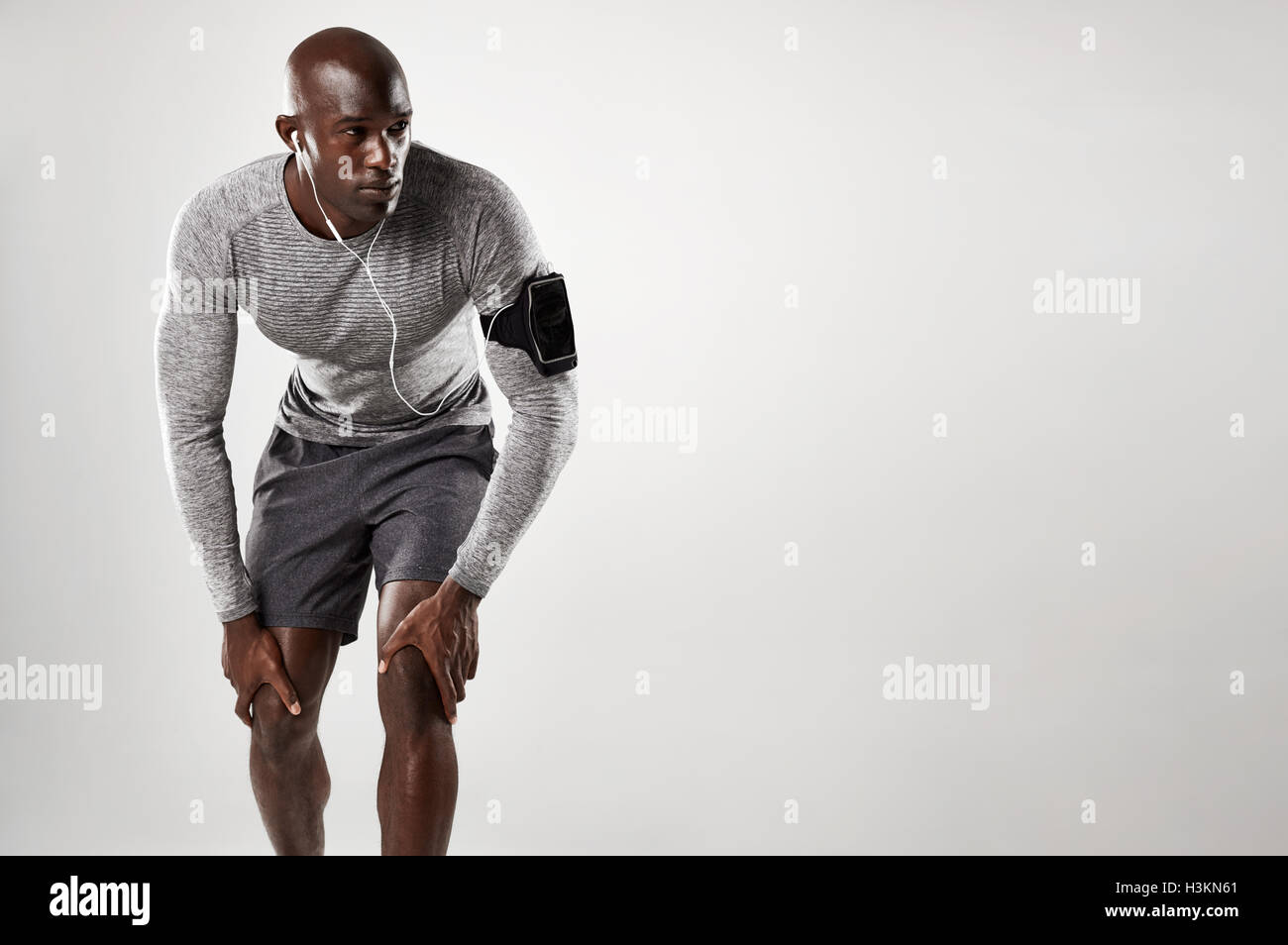 Passen Sie jungen Mann stehend auf grauem Hintergrund und mit Blick auf Textfreiraum. Muskulösen afrikanischen Männermodel Handy-Armbinde tragen ein Stockfoto