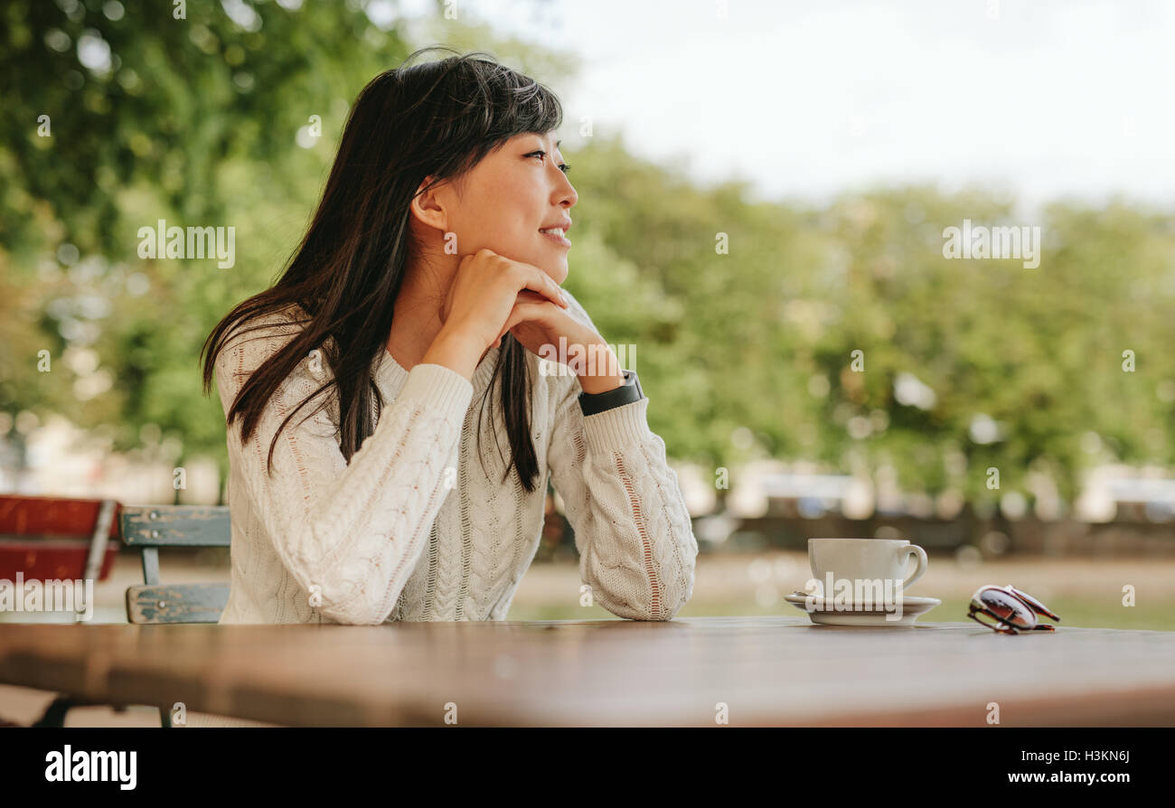 Glückliche junge Frau sitzen im Café bei einer Tasse Kaffee am Tisch und wegsehen. Chinesische Frauen Freizeitgestaltung bei Outdoor-c Stockfoto