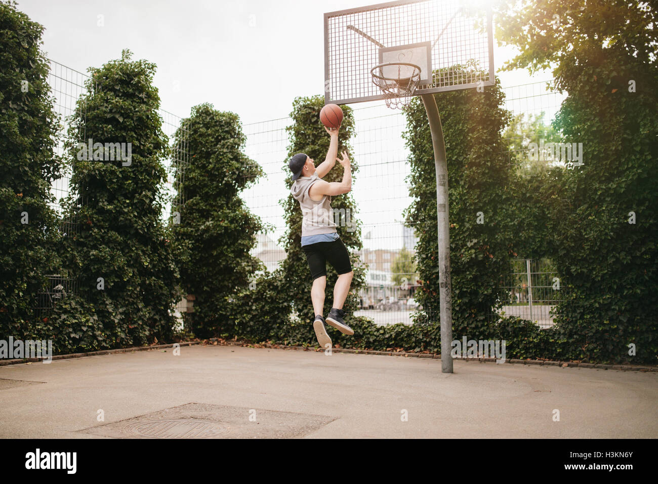 Junger Mann springen und Dunks Basketball in Reifen. Teenager Kerl spielt Streetball. Stockfoto