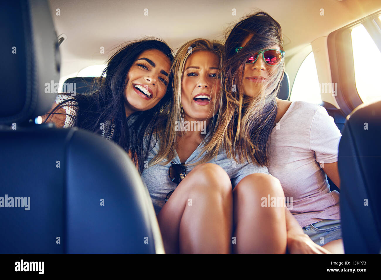 Drei glückliche junge Frauen auf Reisen im Urlaub zusammen zu sitzen, Arm in Arm im Auto Lachen und Lächeln von vorne gesehen se Stockfoto