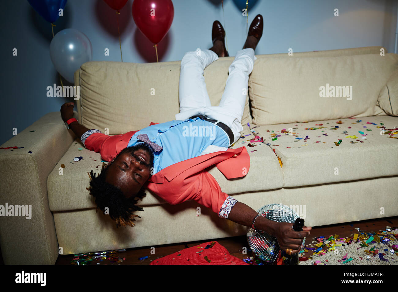 Betrunkener Mann mit Flasche Champagner auf Sofa in unordentlichen Zimmer liegen nach party Stockfoto