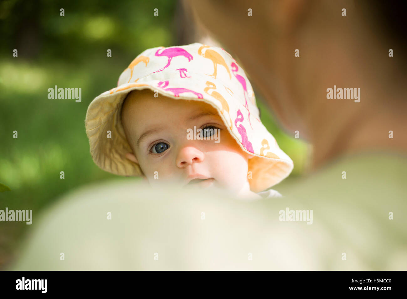 Babymädchen tragen Sonnenhut über Mütter Schulter in die Kamera schaut Stockfoto