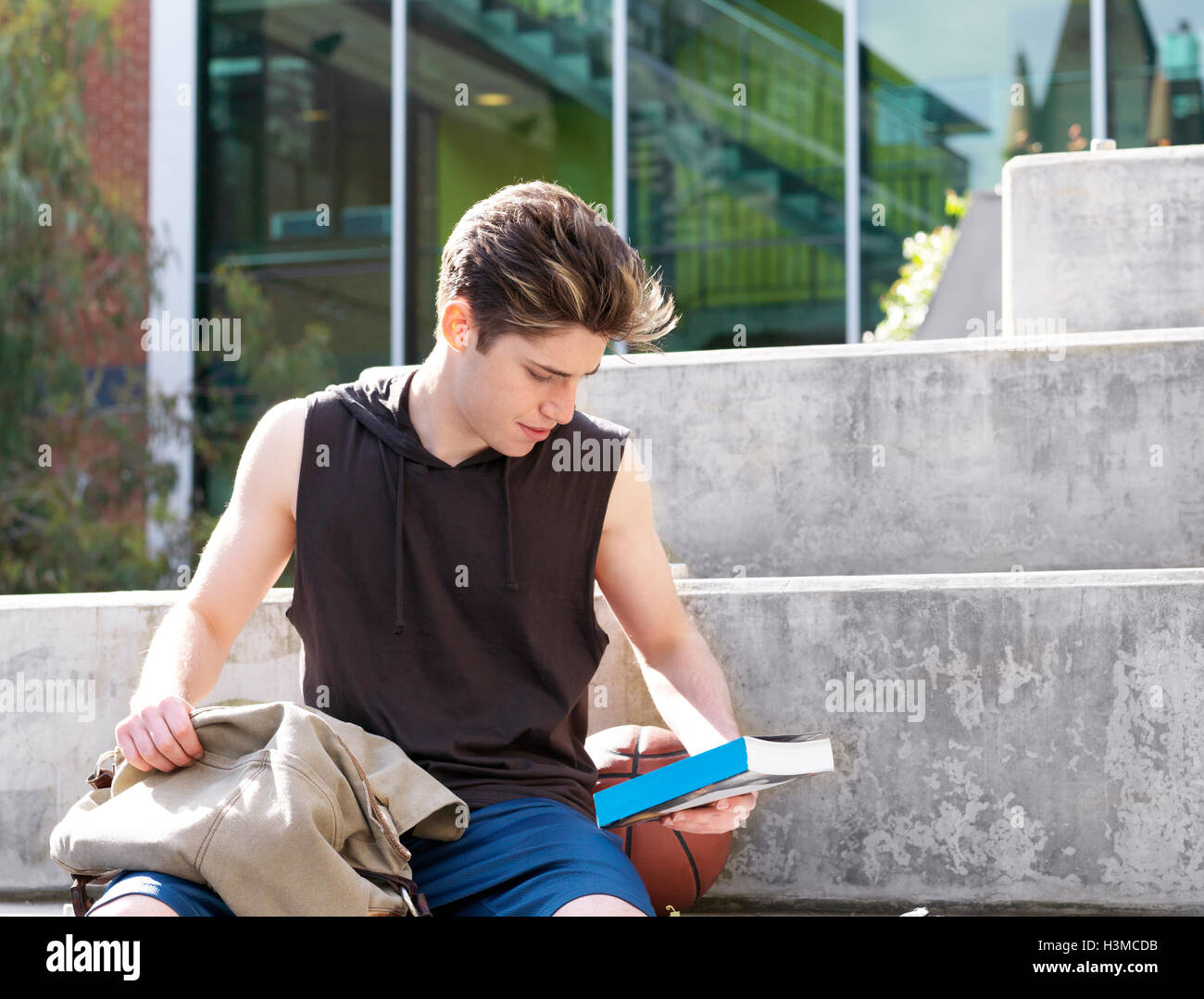 Junger Mann sitzt auf Schritt, im Freien, Rückseite des Buches lesen Stockfoto