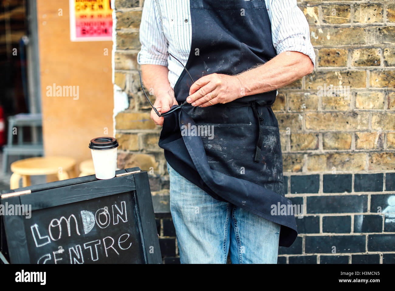 Senior Handwerker außerhalb der Werkstatt, Reinigung von Brillen mit seiner Schürze, Mittelteil Stockfoto