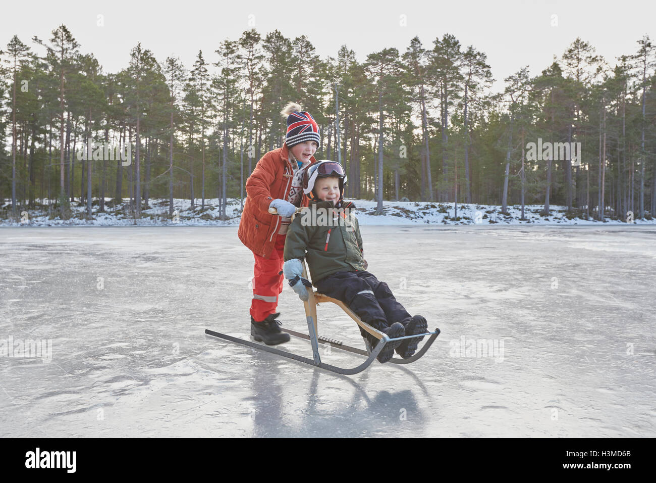 Junge schieben Freund auf Tretschlitten über gefrorenen See, Hotels, Schweden Stockfoto
