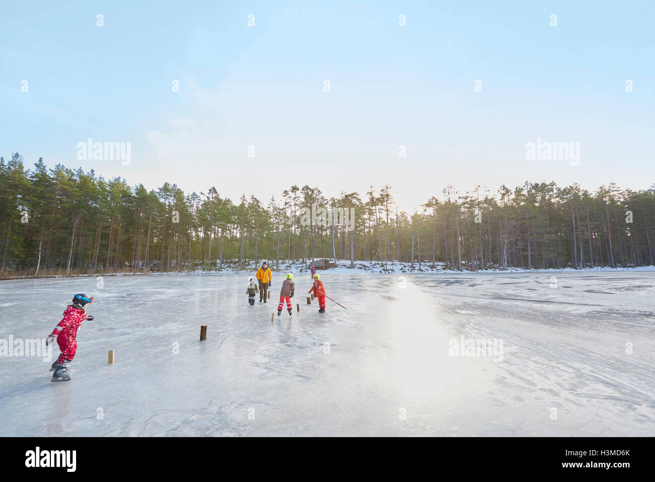 Älteres Paar und Enkel üben Eislaufen Slalom am zugefrorenen See, Hotels, Schweden Stockfoto