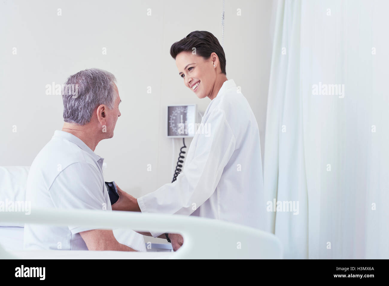 Ärztin mit Blut des Manometers auf älteren männlichen Patienten am Krankenbett Stockfoto