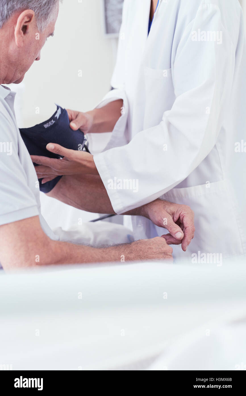 Zugeschnittenen Schuss der Ärztin mit Blutdruck-Messgerät auf älteren männlichen Patienten am Krankenbett Stockfoto