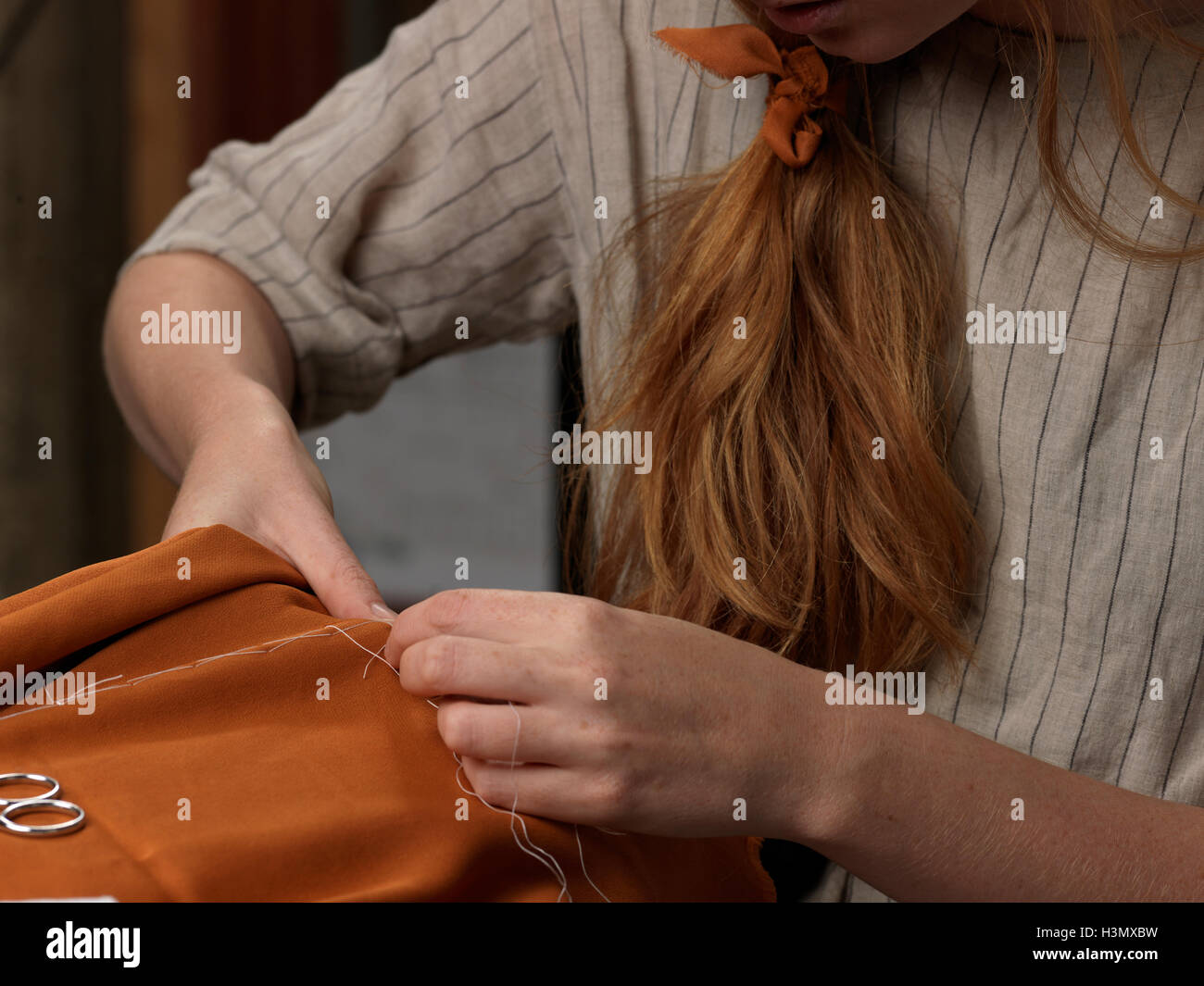 Nahaufnahme von jungen Designerinnen Hände nähen orange Stoff abgeschnitten Stockfoto