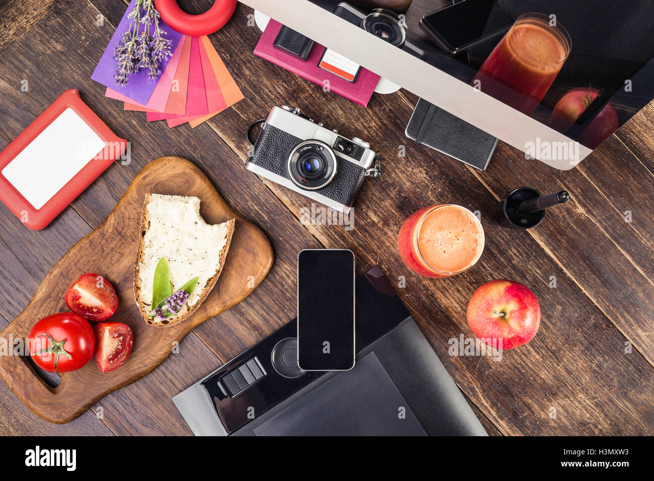 Draufsicht auf Foto-Bearbeitungs-Ausrüstung; Grafiktablett, Retro-Kamera, Smartphone, Desktop-Computer und Mittagessen Stockfoto