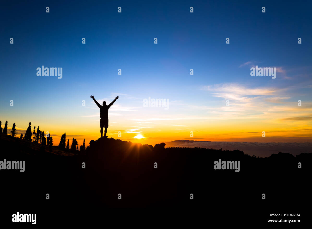 Mann mit Arme ausgestreckt feiert inspirierende Sonnenuntergang in Bergen. Männliche Wanderer oder Bergsteiger mit Händen oben genießen inspir Stockfoto