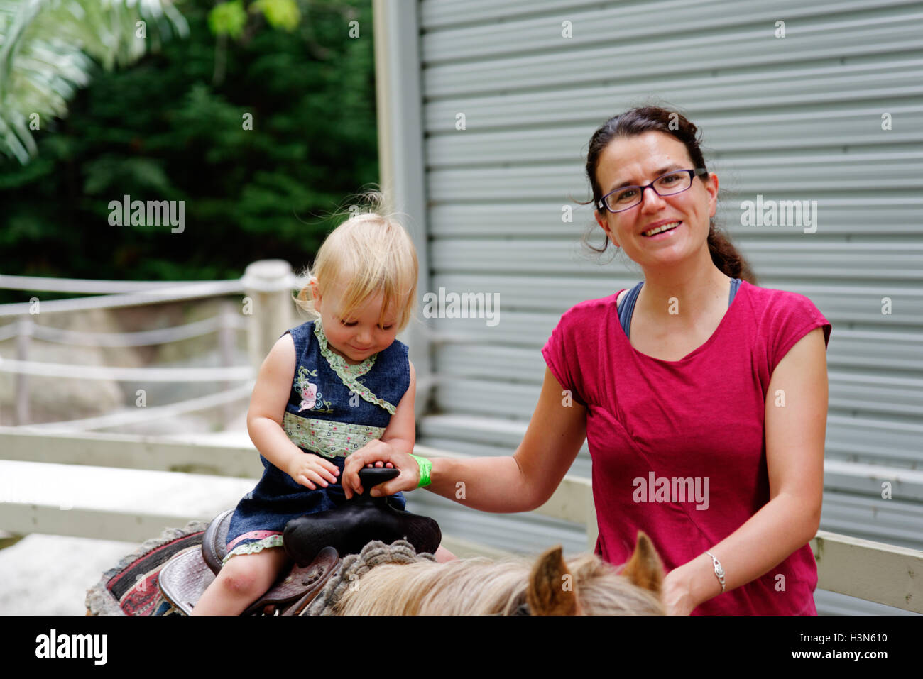 Eine stolze Mama und ihre zwei Jahre alte Tochter auf ihr erstes Ponyreiten Stockfoto