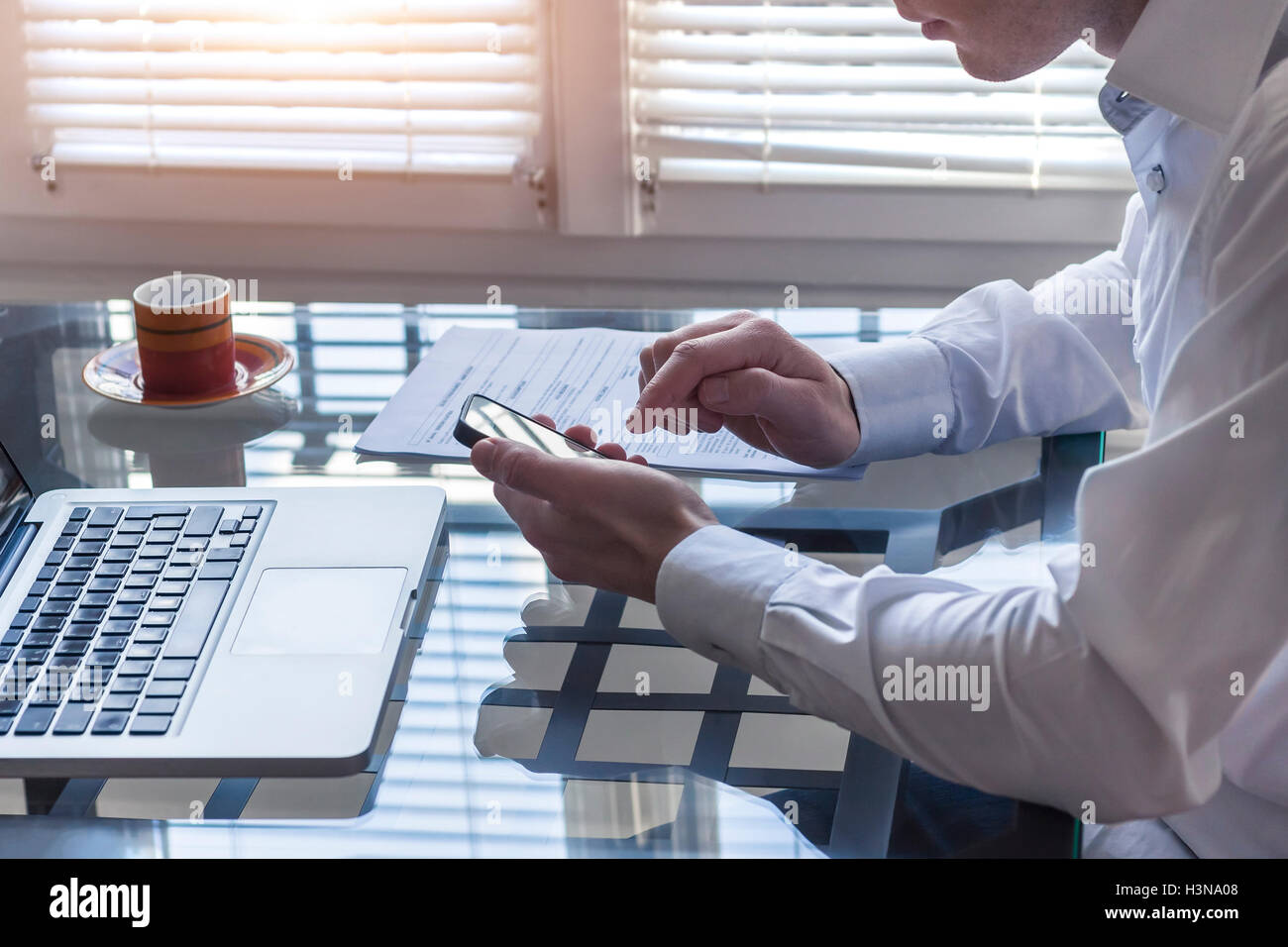 Unternehmer im Büro innen arbeiten mit Handy und Laptop mit einer Tasse Kaffee Stockfoto