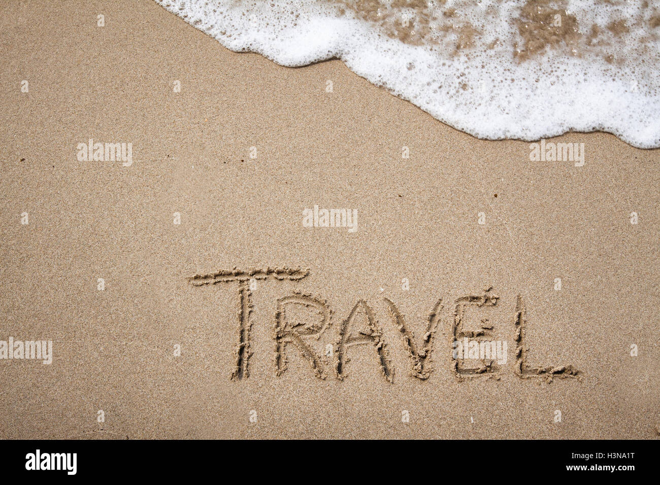Handschrift Reisen Wort auf dem Sand mit einer Welle und Sonnenlicht Stockfoto