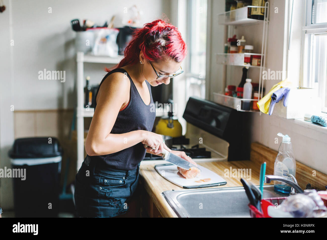 Junge Frau mit rosa Haaren schneiden Fleisch in Küche Stockfoto