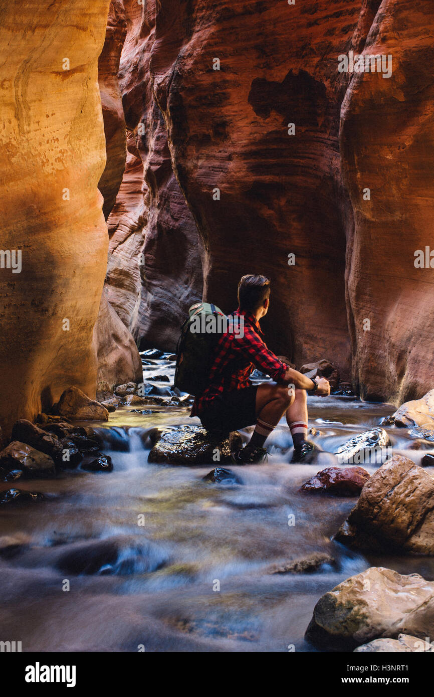 Männliche Wanderer sitzen in Höhle auf dem Flussfelsen, Zion Nationalpark, Utah, USA Stockfoto