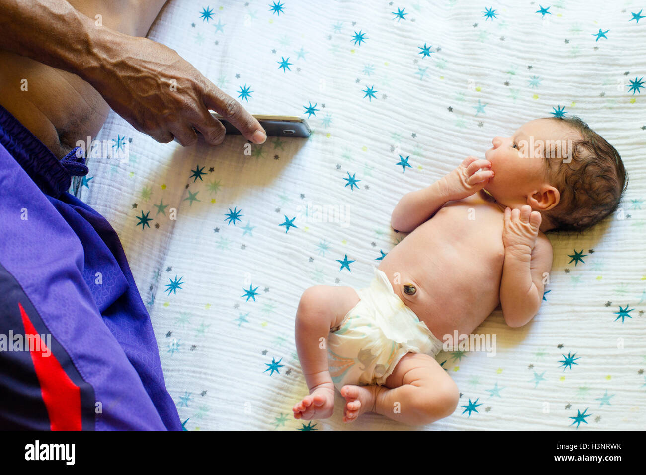 Neugeborenes Baby Boy auf Bett neben Vater mit smartphone Stockfoto
