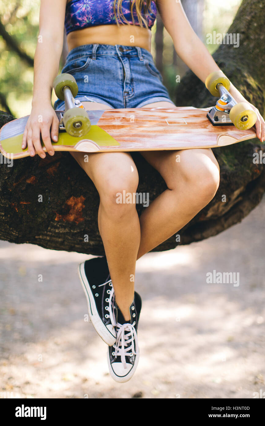 Frau mit Skateboard sitzt auf Baum Stockfoto