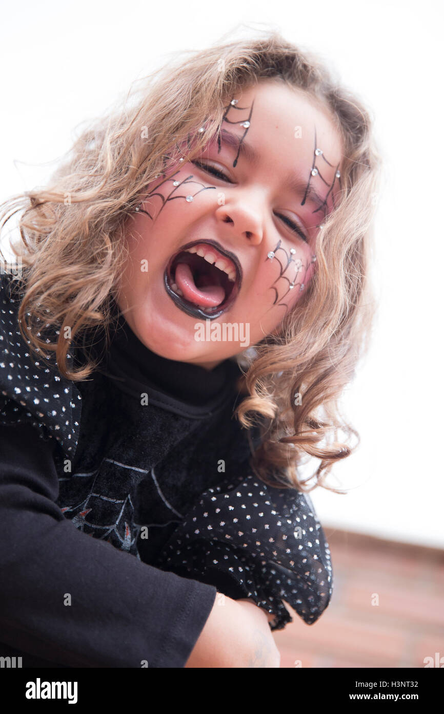 Gruselige kleine Mädchen in schwarz Halloween-Kostüm und lackierten Webs auf Gesicht mit offenem Mund. Stockfoto