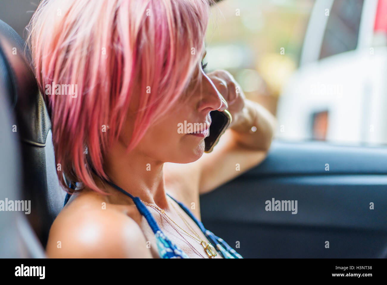 Reife Frau mit rosa Haaren, sitzt hinter dem Auto, mit smartphone Stockfoto