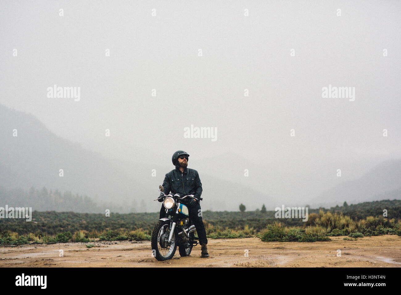 Motorradfahrer mit Helm sitzt auf dem Motorrad wegsehen, Kennedy Meadows, Kalifornien, USA Stockfoto