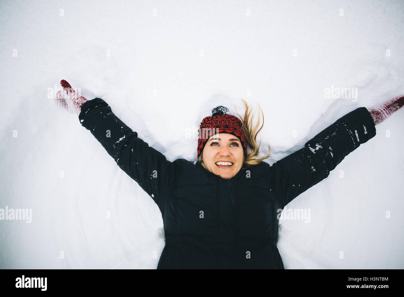 Frau liegt auf dem Rücken im Schnee Arme öffnen Stockfoto