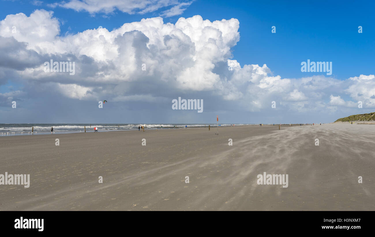 Menschen, die genießen einen Spaziergang an einem Sandstrand an der Nordsee unter hoch aufragenden weißen Cumulus Wolke Formationen am blauen Himmel Stockfoto