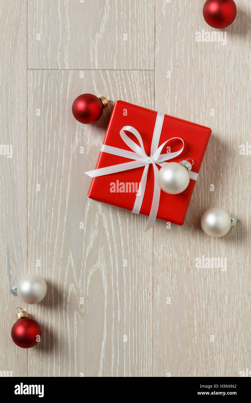 Weihnachtsgeschenk auf rustikalen Holz Hintergrund vorhanden. Einfach, klassisch rot verpackt Geschenkbox mit Schleife und Ornamente Stockfoto