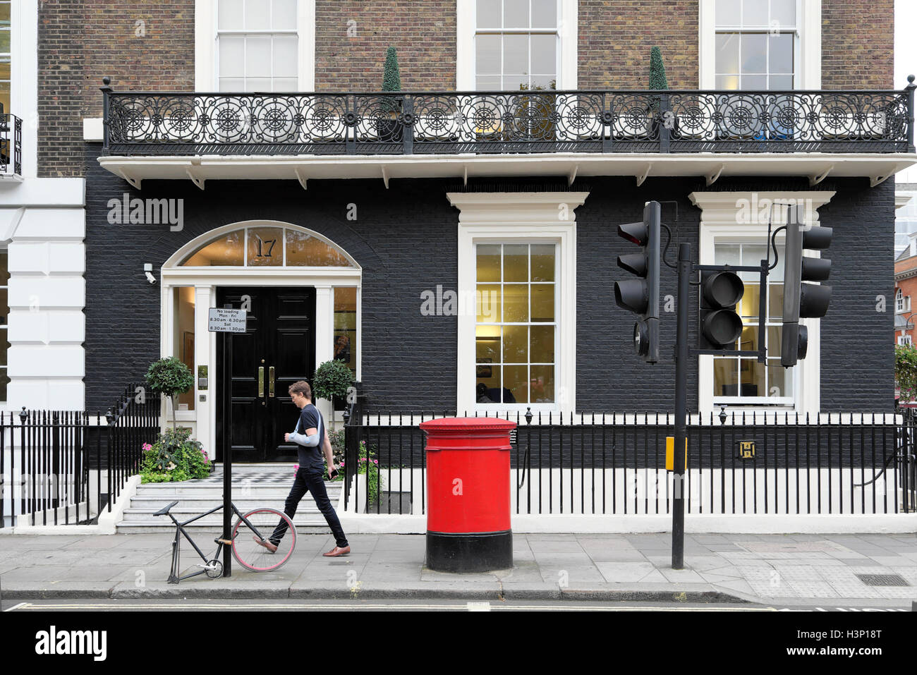 Ein Mann mit Arm in Cast, der am Harley Street Medical Center vorbeiläuft, roter Briefkasten und verriegeltem Fahrradrahmen mit einem Rad W1G London England UK KATHY DEWITT Stockfoto