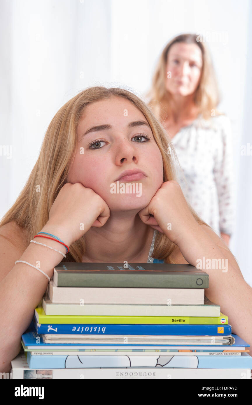 -MODELL VERÖFFENTLICHT. Teenager-Mädchen stützte sich auf Ellbogen mit Textbüchern, Mutter, die gerade im Hintergrund. Stockfoto