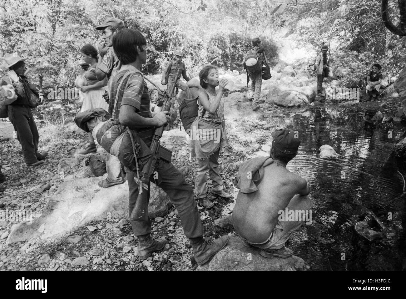 CHALATENANGO, EL SALVADOR, FEB 1984: - innerhalb der FPL Zonen Control A Guerillagruppe FPL-Männer und Frauen Kämpfer Rest und nehmen Wasser aus einem Stream. Stockfoto