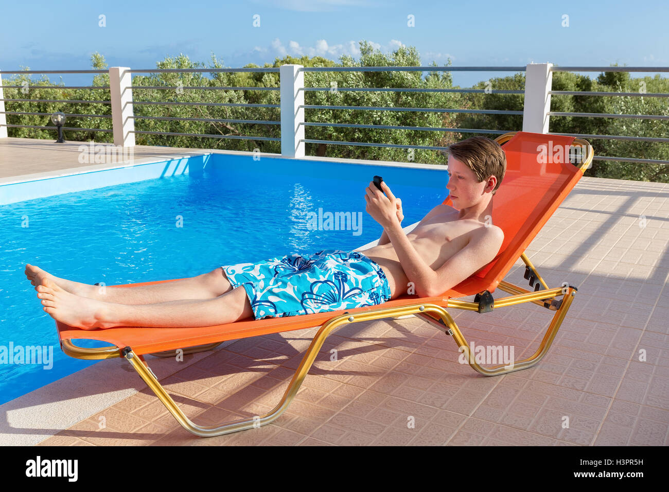Kaukasische Youngster auf Sonnenliege Betrieb Handy am Pool liegend Stockfoto
