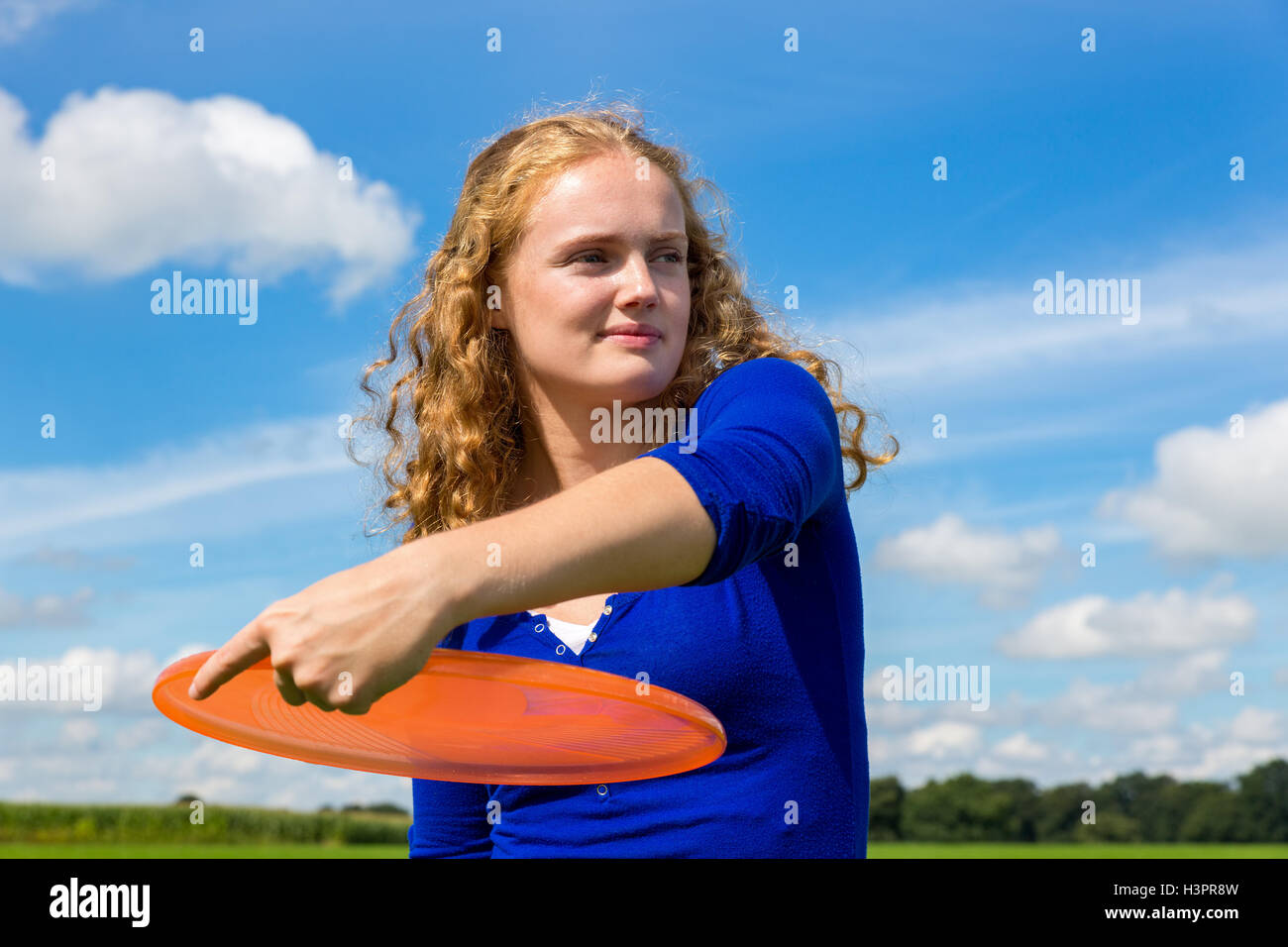 Kaukasische Mädchen hält orange Frisbee im freien gegen blauen Himmel Stockfoto
