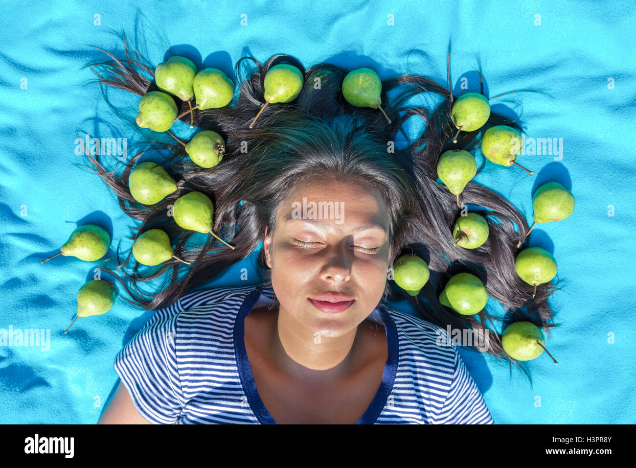 Junge Frau liegt auf Decke Augen geschlossen grüne Birnen in Schwarzes Haar Stockfoto