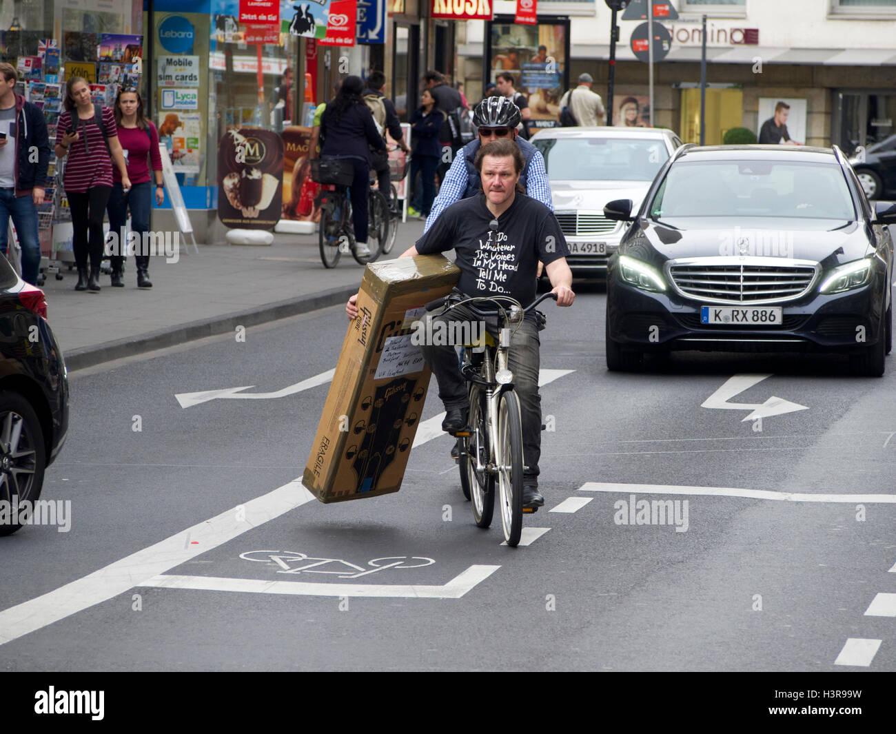 Mann, Radfahren auf den Straßen von Köln mit neuen Gibson-Gitarre und einige Transportprobleme zu lösen. Deutschland Stockfoto