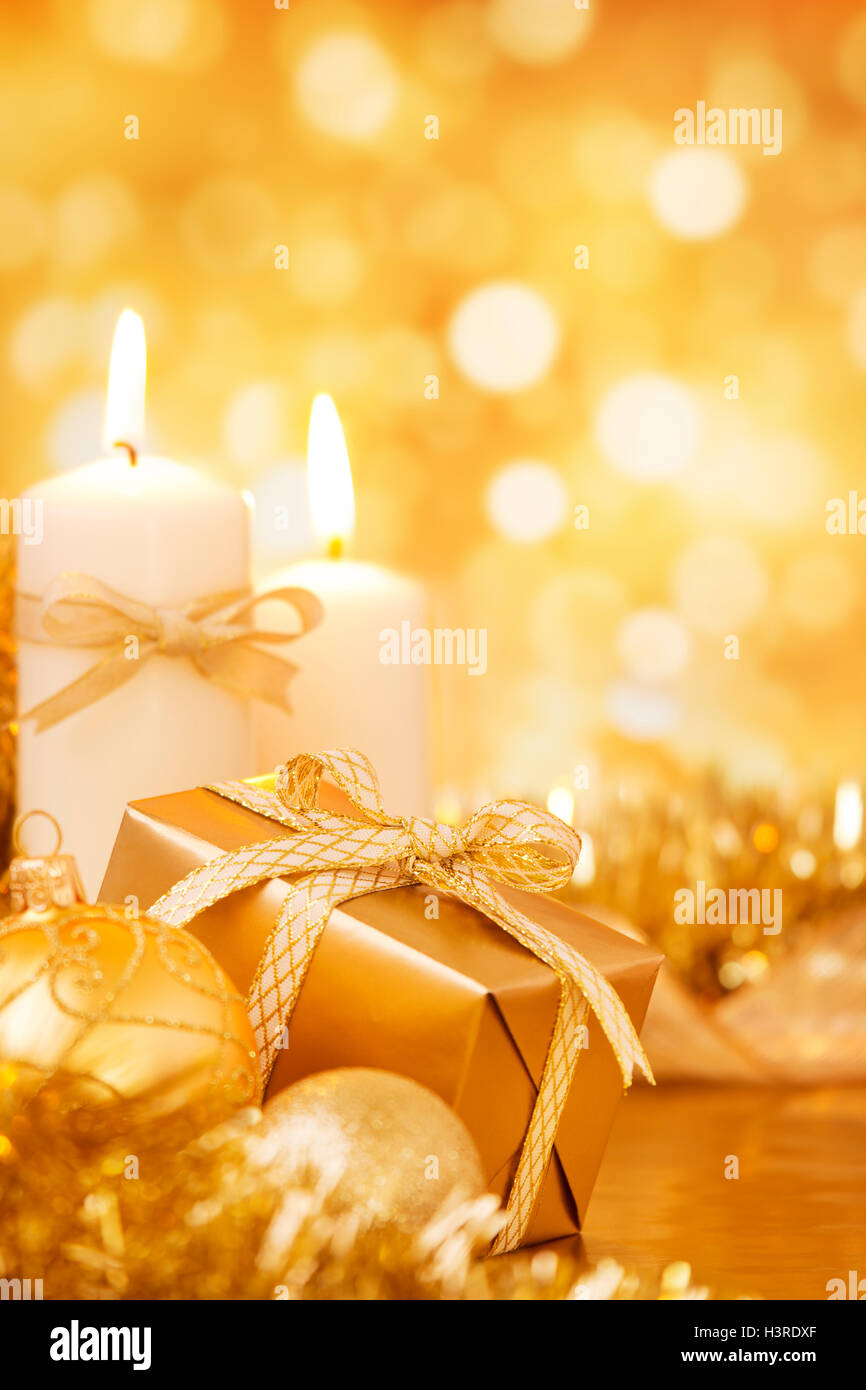 Goldene Christbaumkugeln, Kerzen und ein Geschenk auf einer hell glitzernden gold Hintergrund. Stockfoto