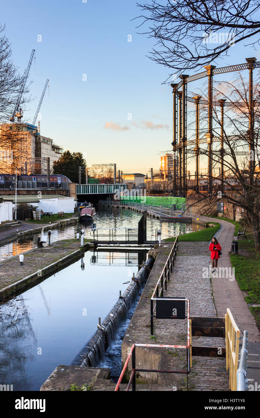 Frau in einem roten Mantel Wandern auf dem Leinpfad des Regent's Canal in St. Pancras Lock, London, Großbritannien, ein Eurostar und Gasometer im Hintergrund, 2014 Stockfoto