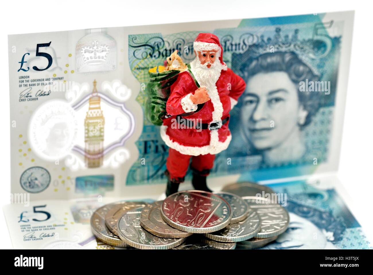 Ein Weihnachtsmann Figur stand vor einigen neuen fünf-Pfund-Banknoten und Münzen. England-UK. Stockfoto