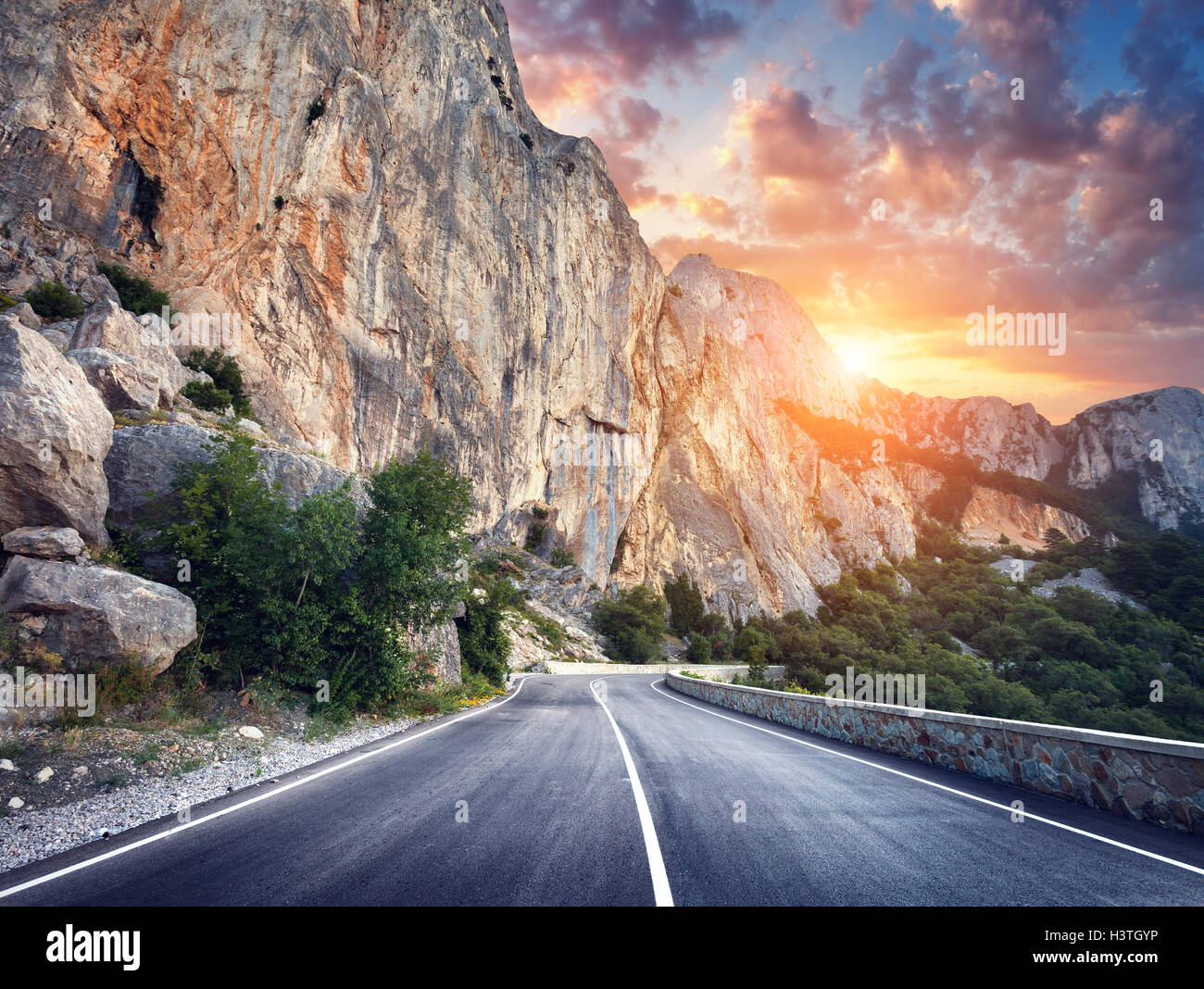 Schöne asphaltierte Straße. Bunte Landschaft mit hohen Felsen, Bergstraße mit perfekter Asphalt, Bäume, Sonne und erstaunliche bewölkt Stockfoto