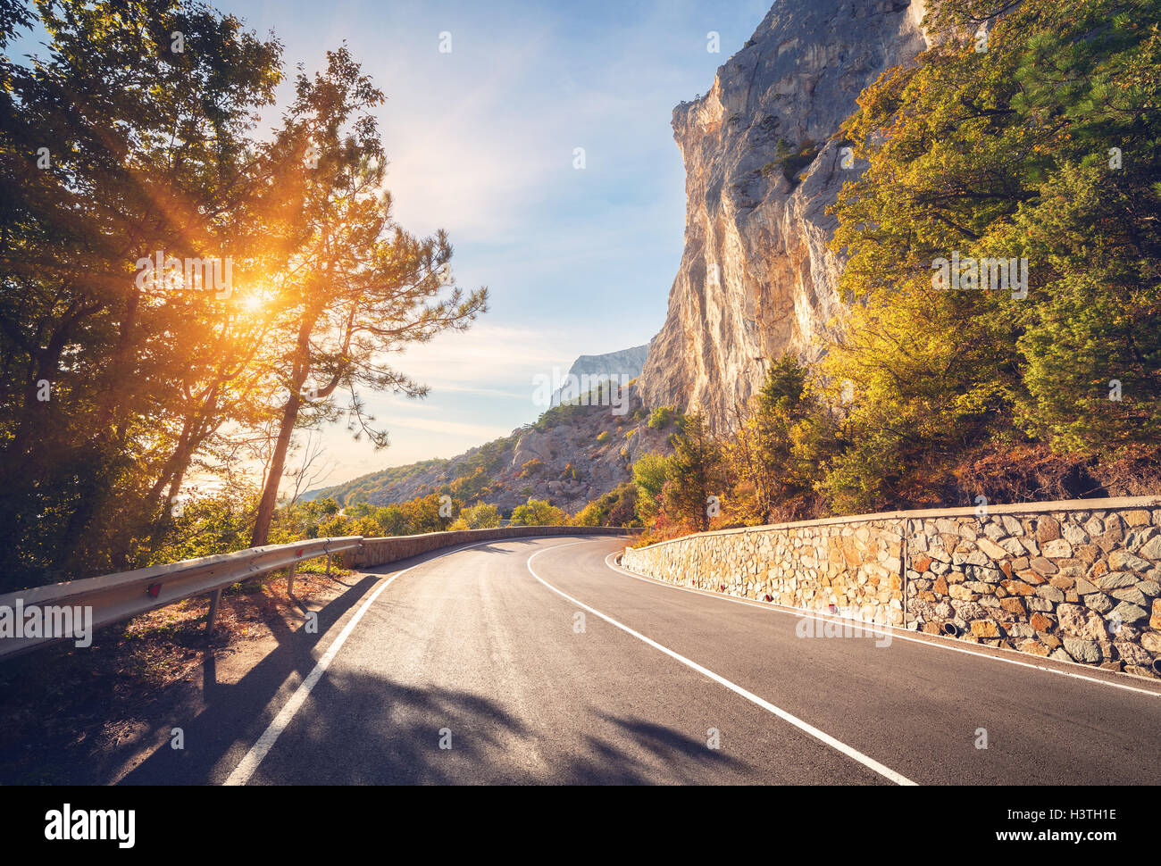 Asphaltierte Straße. Bunte Landschaft mit schönen Bergstraße mit perfekter Asphalt. Hohe Felsen, Bäume, blauer Himmel bei Sonnenaufgang Stockfoto