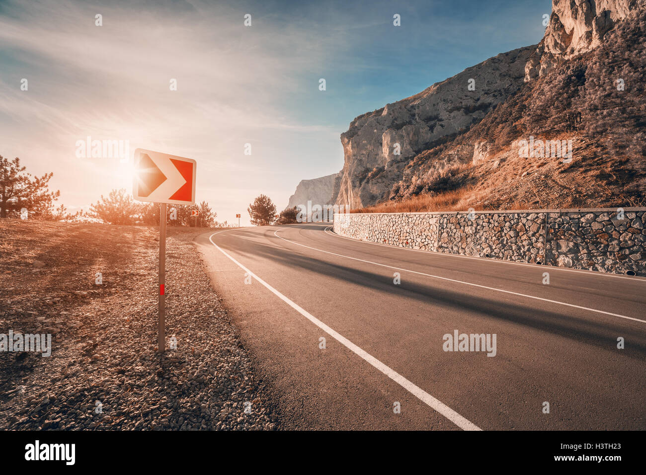 Asphaltierte Straße und Straßenschild in Bergen bei Sonnenaufgang mit Vintage Muskelaufbau. Wunderschöne Landschaft mit Berg Autobahn, Verkehrszeichen Stockfoto