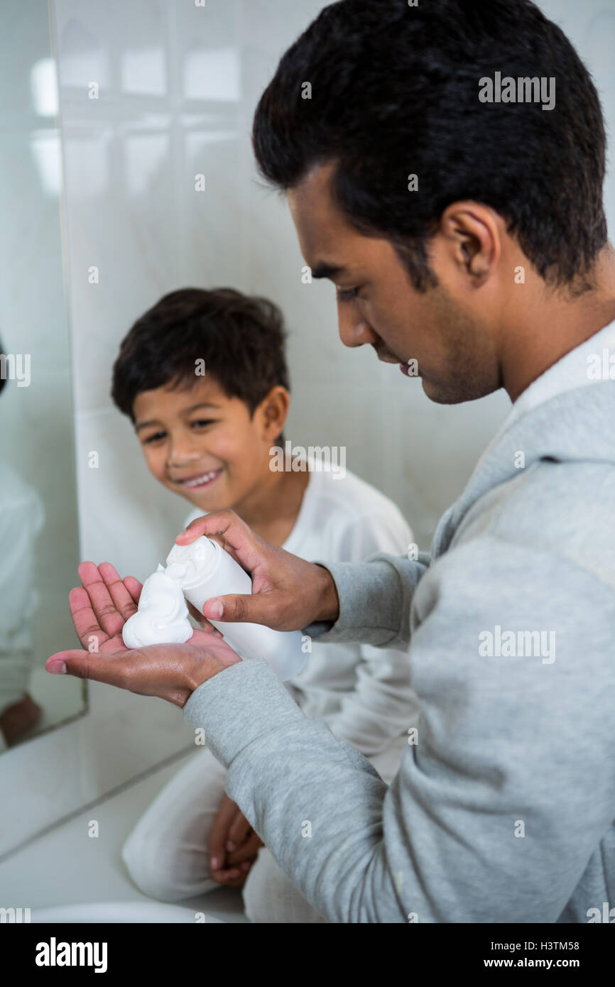 Sprühen Rasierschaum auf Seite während Sohn sucht Vater Stockfoto