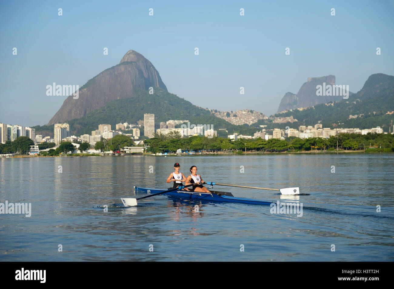 Zwei junge Frauen in den frühen Morgenstunden Rudern Training in der Lagoa Rodrigo de Freitas Lagune, mit Rio De Janeiro Stockfoto