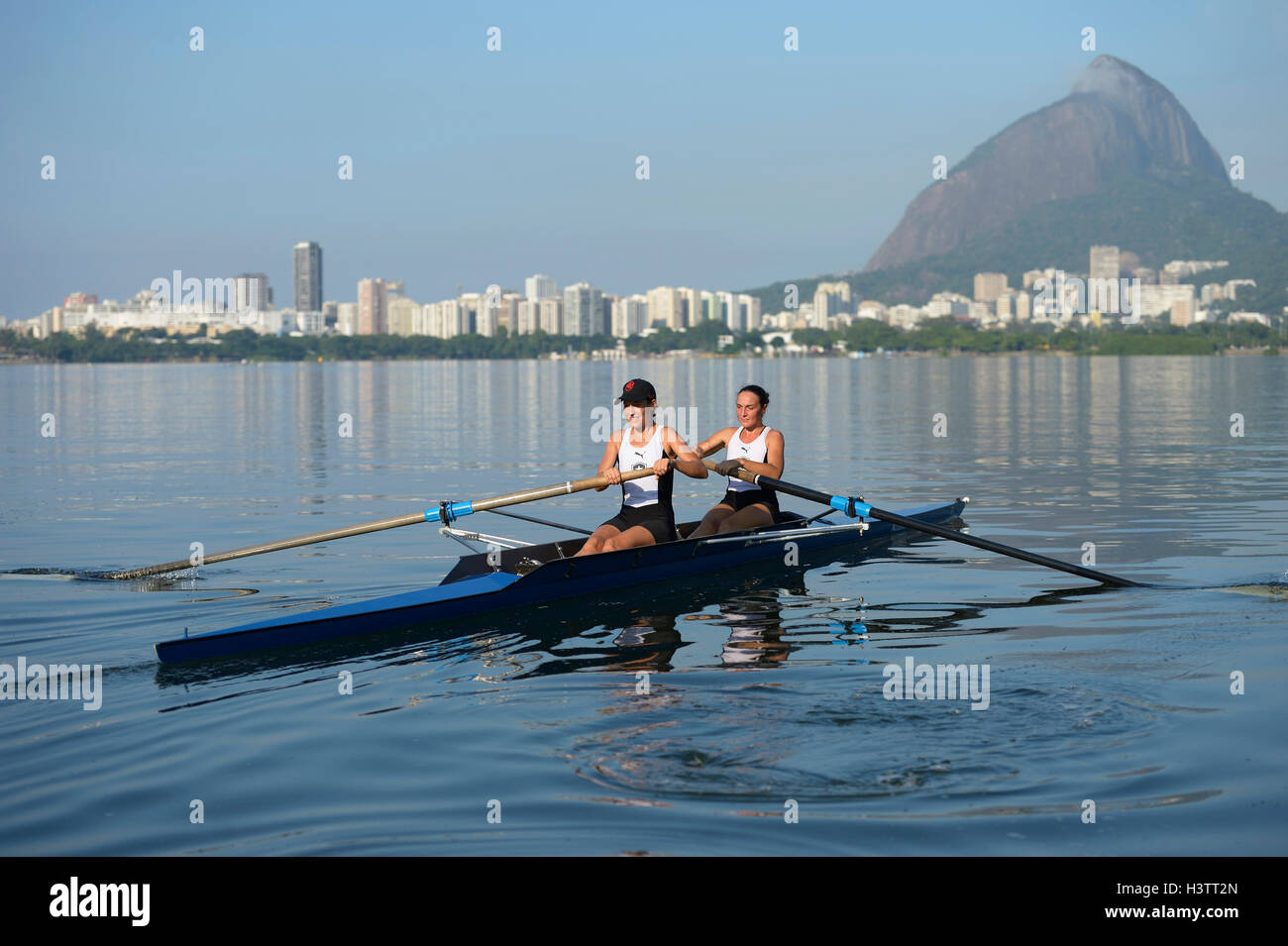 Zwei junge Frauen in den frühen Morgenstunden Rudern Training in der Lagoa Rodrigo de Freitas Lagune, mit Rio De Janeiro Stockfoto