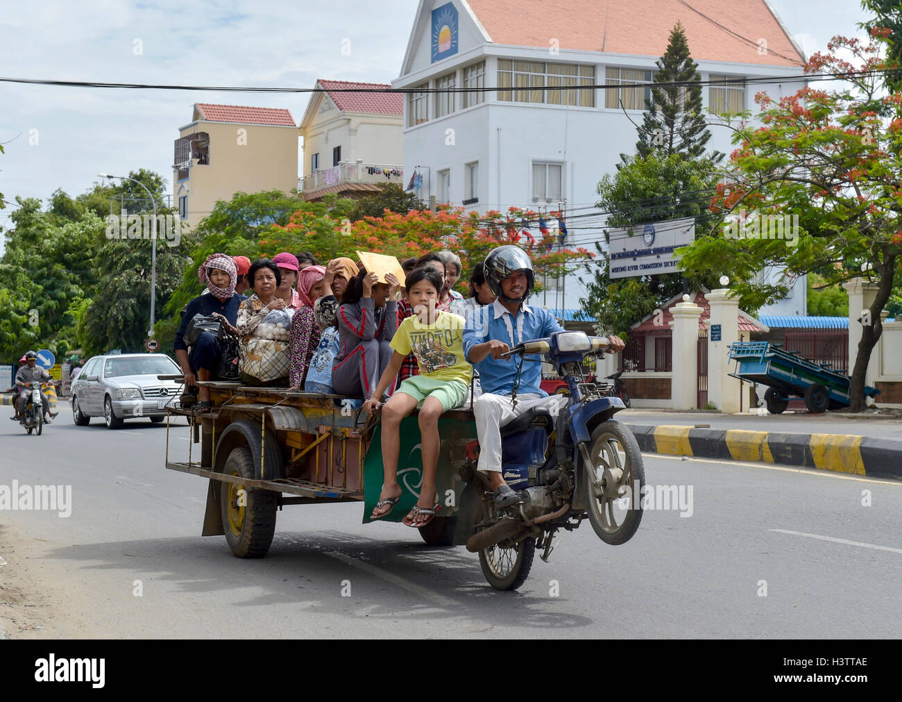 Mann auf Roller macht einen Wheelie, Anhänger beladen mit vielen Menschen, Phnom Penh, Kambodscha Stockfoto