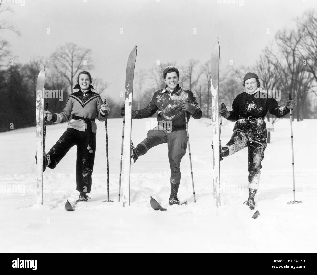 1930ER JAHREN ZWEI FRAUEN UND EIN MANN, DER BLICK IN DIE KAMERA LÄCHELT, POSIERT AUF SKIERN MIT PASSENDEN SKI STELLTE SICH AUFRECHT Stockfoto