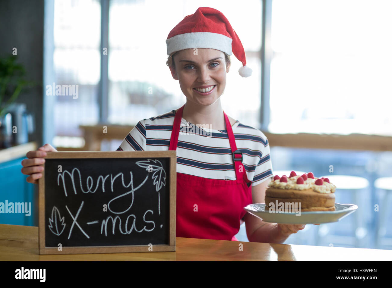 Porträt der Kellnerin mit Schiefer mit merry x-mas-Zeichen und Kuchen im café Stockfoto
