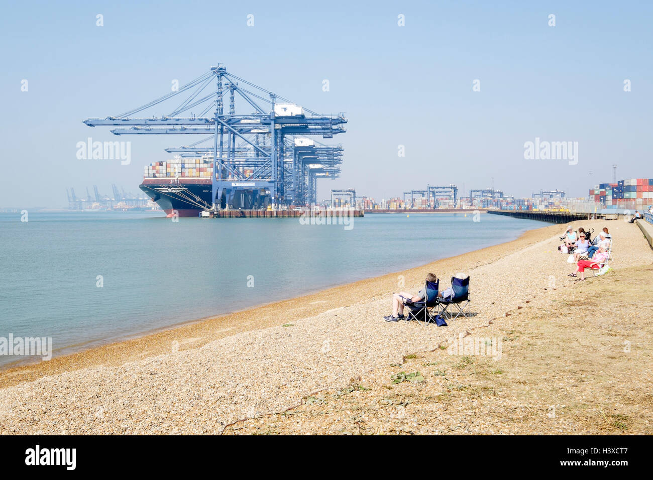 Sonnenanbeter entspannen am Strand. Venedig MSC Containerschiff im Hafen von Felixstowe, Suffolk, UK im Hintergrund verankert. Stockfoto