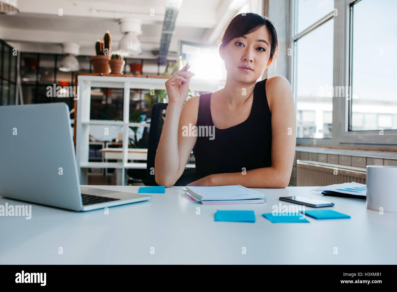 Porträt der selbstbewusste junge Frau sitzt an ihrem Schreibtisch mit Laptop und Klebstoff Noten Blick in die Kamera. Asiatische Geschäftsfrau Arbeit Stockfoto