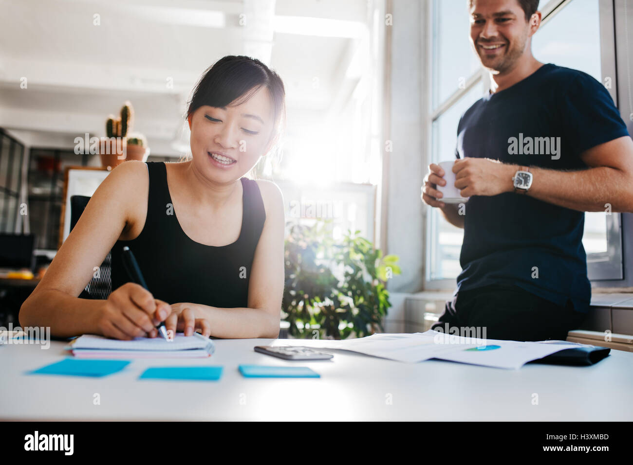 Junge asiatische Frau Schreiben von Notizen mit männlicher Kollege mit Tasse Kaffee bereit. Kollegen zusammen arbeiten im Büro Stockfoto